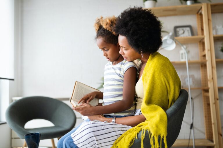 Little girl reading book with mother at home