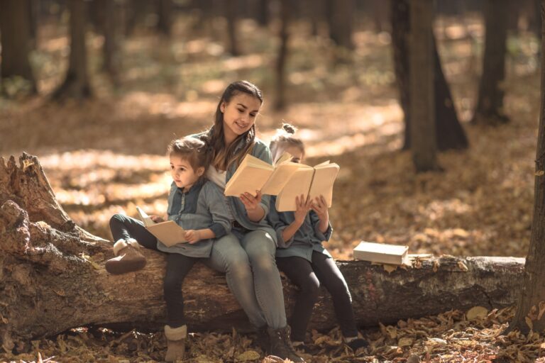 Mother reading a book to children in the woods.