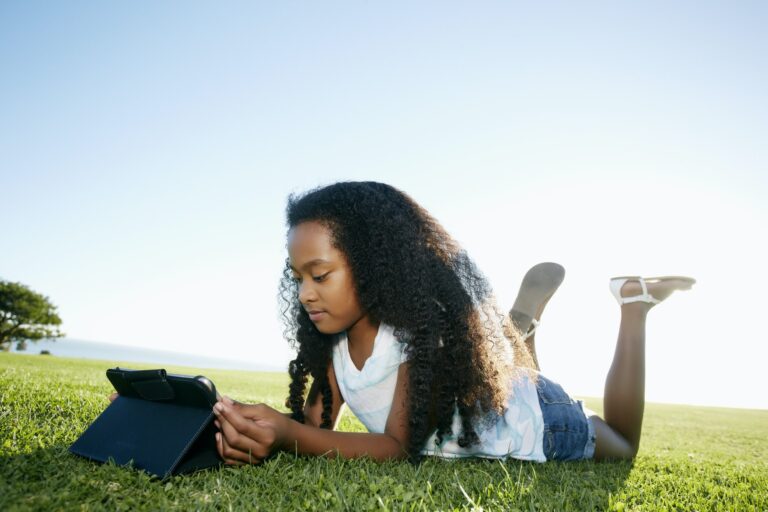 level four aged mixed race girl lying on grass looking at a digital tablet.